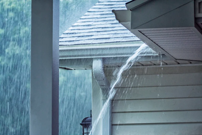 Heavy rain overflowing a roof gutter onto the side of a house