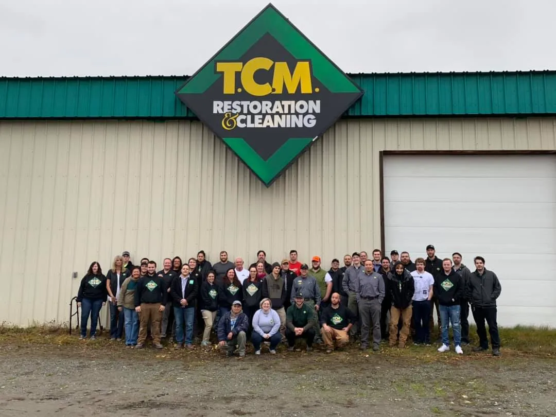 The TCM Restoration team gathered outside the company facility under the TCM Restoration and Cleaning sign